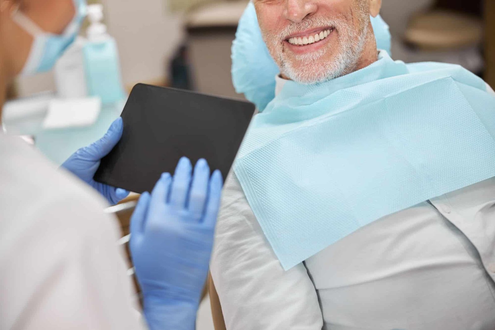 Senior gentleman smiling at the dentist holding a tablet